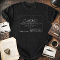 Black t-shirt with UFO blueprint design of a UFO craft on a wooden surface with vintage items.
