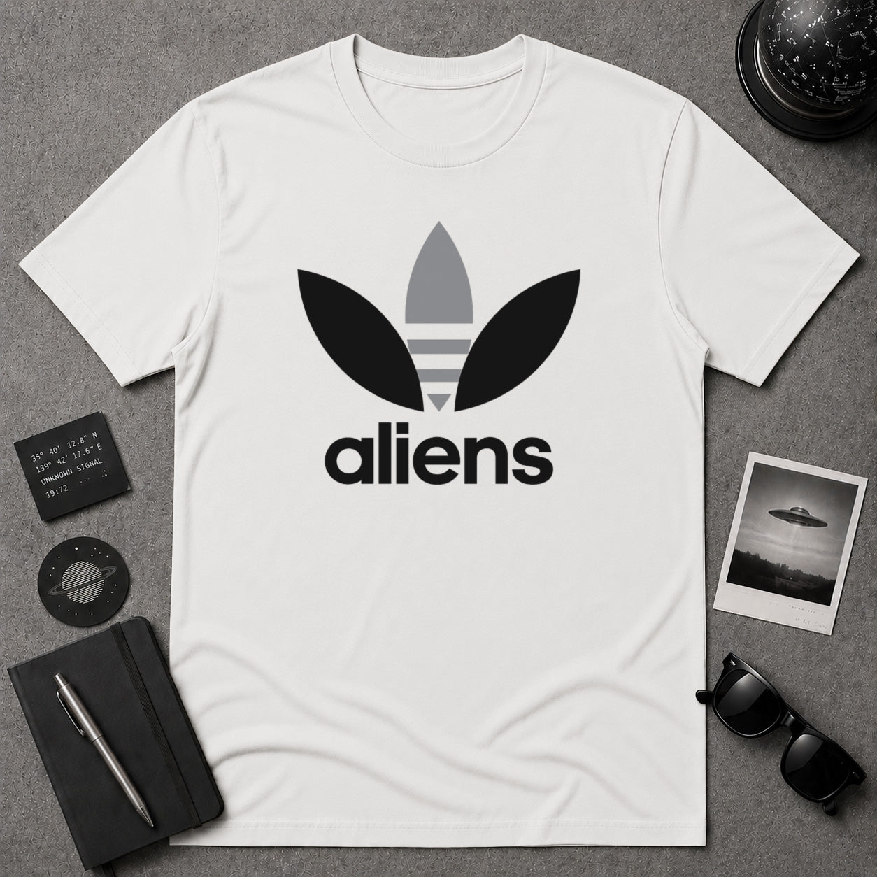 A white short-sleeve t-shirt with a black and gray alien-themed logo on the chest, visually reminiscent of the classic Adidas logo. This is a parody shirt.